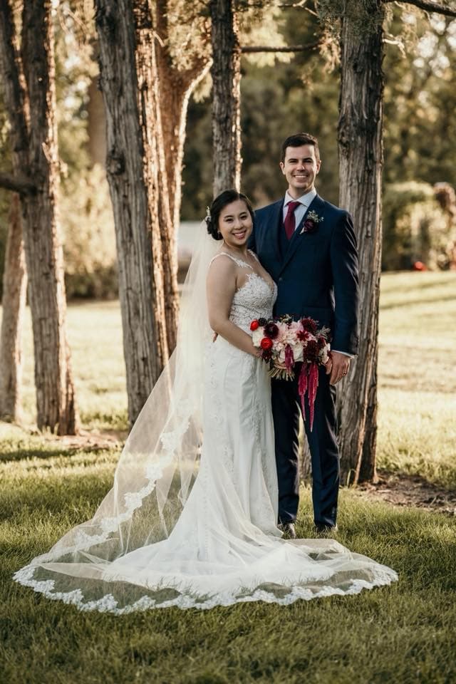Megan and Austin in wedding attire under a row of trees.