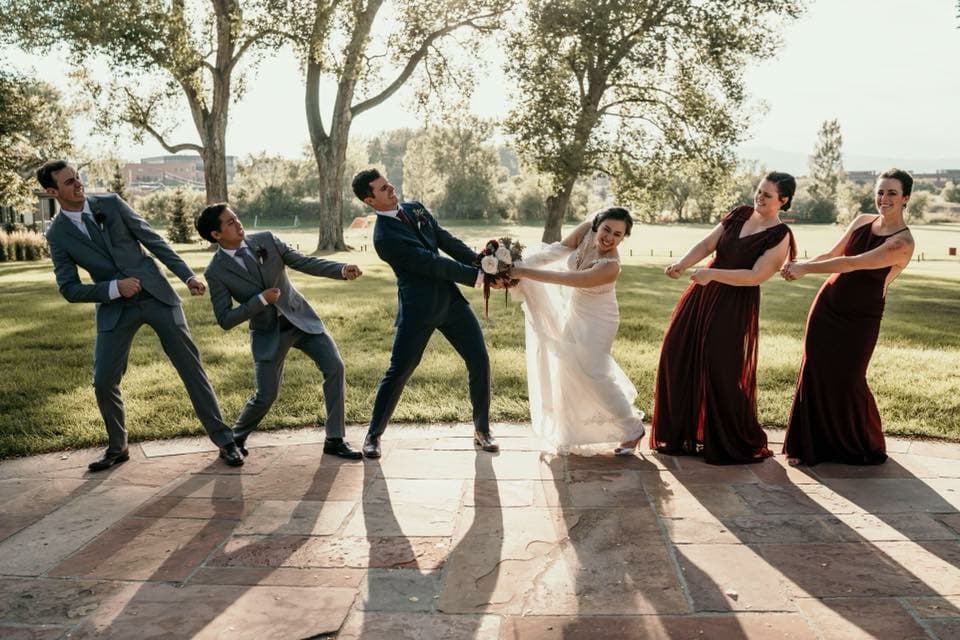 Wedding party in a tug-of-war pose, the bride being pulled toward the groomsmen and the bridesmaids holding the line.