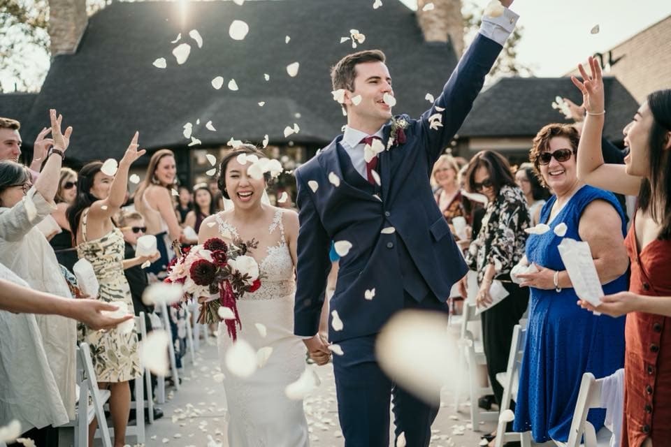 Megan and Austin walking down the aisle as guests throw white rose petals at their wedding.